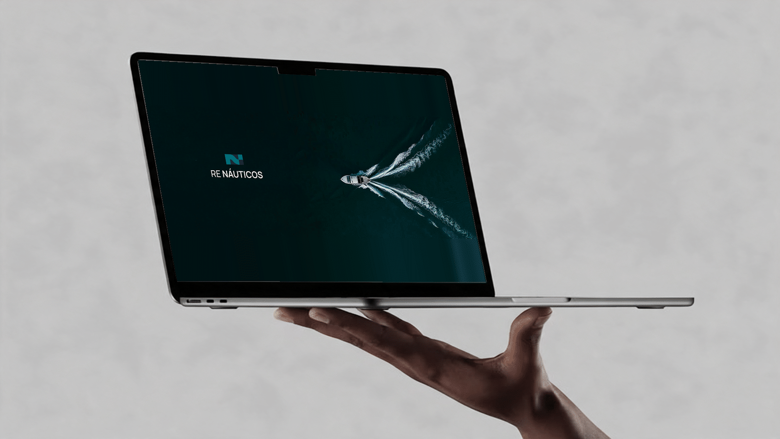A hand holds a laptop displaying the Re Náuticos brandbook: logo, typography, colors, icons, photography and brand applications.